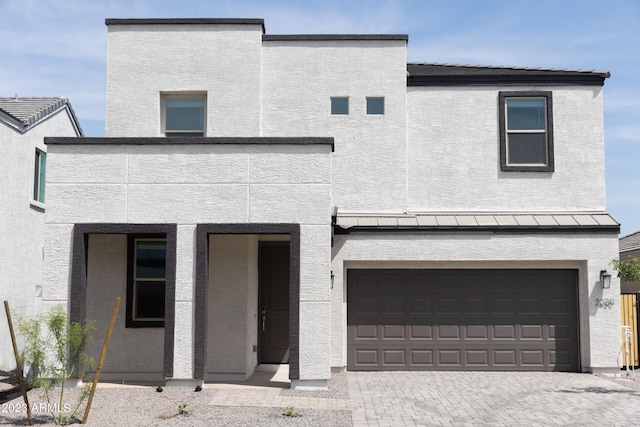 view of front of property with metal roof, an attached garage, a standing seam roof, decorative driveway, and stucco siding