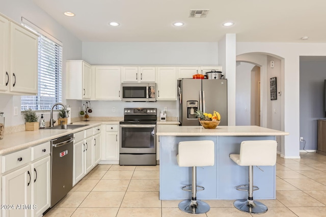 kitchen with white cabinetry, sink, a breakfast bar area, a kitchen island, and appliances with stainless steel finishes