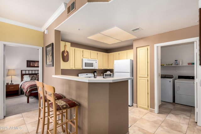 kitchen with light tile patterned floors, white appliances, a breakfast bar area, and visible vents