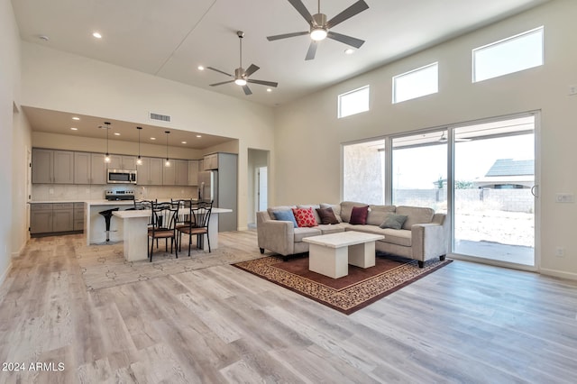 living room with a high ceiling, light hardwood / wood-style flooring, and ceiling fan