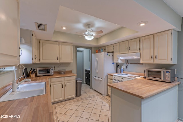 kitchen featuring white appliances, wood counters, a tray ceiling, under cabinet range hood, and a sink