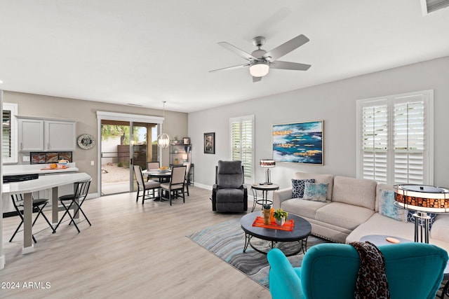 living room featuring a wealth of natural light, ceiling fan with notable chandelier, and light wood-type flooring