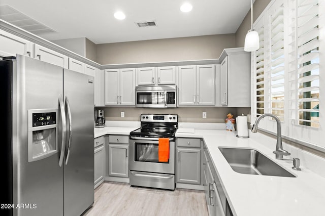 kitchen with gray cabinetry, hanging light fixtures, sink, light hardwood / wood-style flooring, and appliances with stainless steel finishes