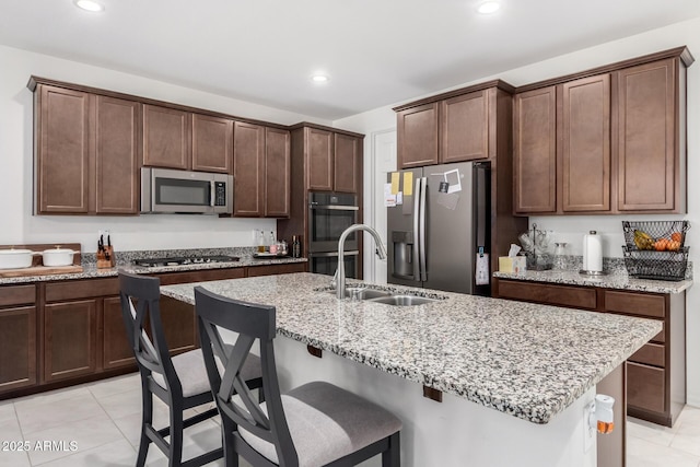 kitchen with sink, light tile patterned floors, an island with sink, stainless steel appliances, and light stone countertops