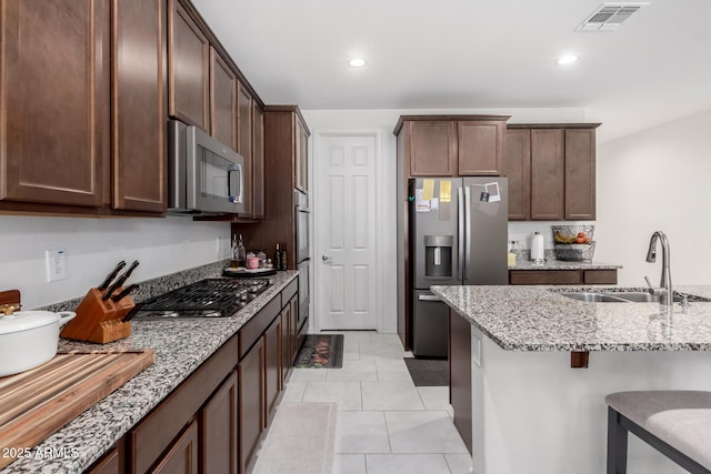 kitchen featuring sink, a breakfast bar area, light tile patterned floors, stainless steel appliances, and light stone countertops