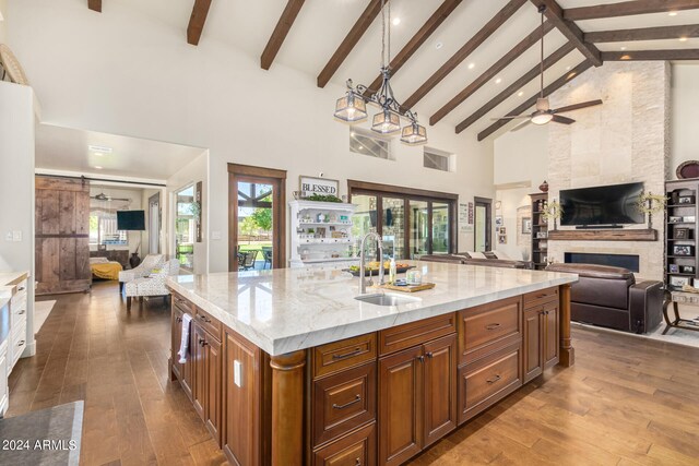 kitchen with a kitchen island with sink, a large fireplace, sink, high vaulted ceiling, and hardwood / wood-style flooring