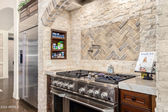 kitchen with premium appliances, light stone countertops, dark brown cabinetry, and dark wood-type flooring