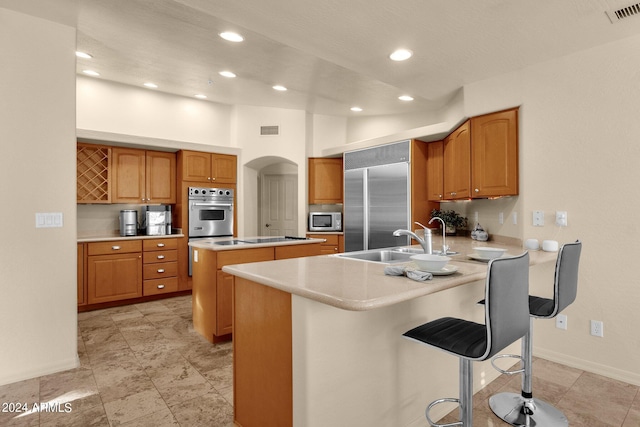 kitchen featuring built in appliances, a kitchen breakfast bar, a center island, kitchen peninsula, and sink