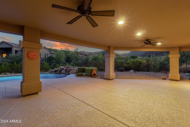 patio terrace at dusk featuring a fenced in pool and ceiling fan