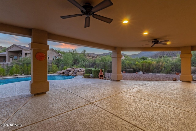 patio terrace at dusk with ceiling fan, a fenced in pool, and a mountain view