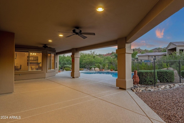 patio terrace at dusk with a fenced in pool and ceiling fan