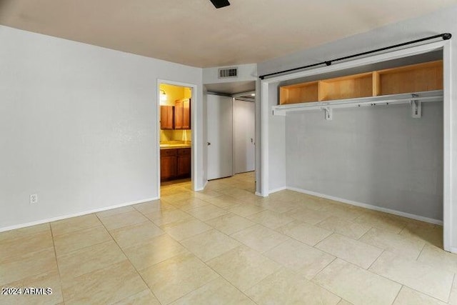 unfurnished bedroom with a closet, light tile patterned floors, and ensuite bath