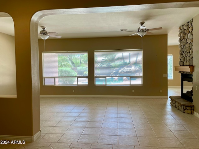 tiled empty room with ceiling fan and a stone fireplace