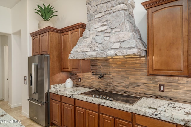 kitchen with high end fridge, light stone counters, black electric cooktop, and decorative backsplash