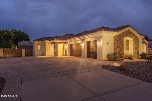 mediterranean / spanish house featuring an attached garage, stone siding, a tile roof, and concrete driveway