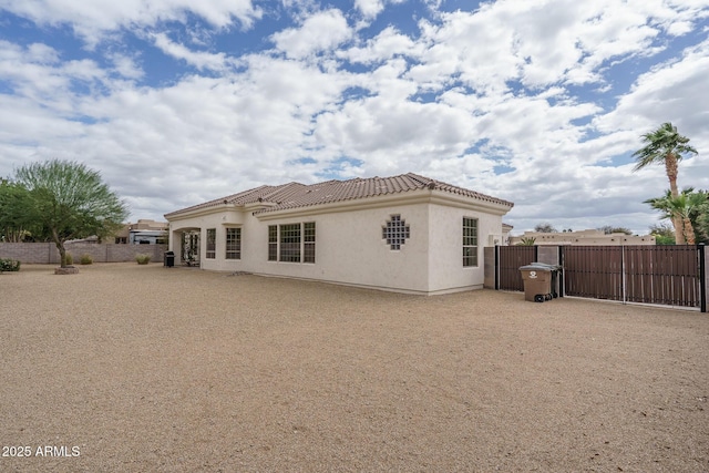 rear view of house featuring a gate, a tile roof, fence, and stucco siding