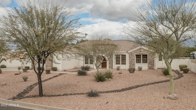 view of front facade featuring stone siding, a tile roof, fence, and stucco siding