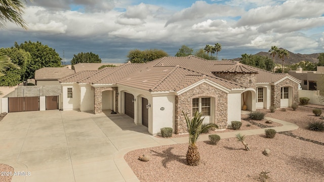 mediterranean / spanish-style home featuring driveway, stone siding, a tiled roof, an attached garage, and stucco siding