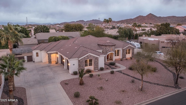 view of front of property featuring concrete driveway, stone siding, a tiled roof, a mountain view, and stucco siding