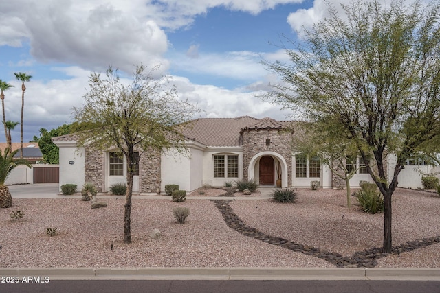 mediterranean / spanish home featuring stone siding, fence, stucco siding, and a tiled roof