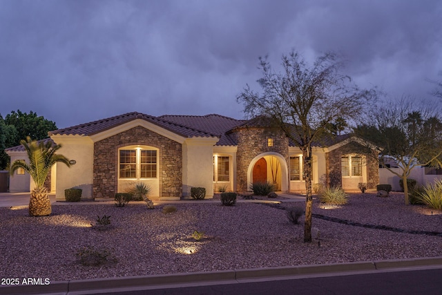 mediterranean / spanish-style home with stone siding, a tile roof, and stucco siding