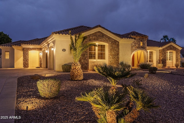 mediterranean / spanish-style house with stone siding, driveway, and stucco siding