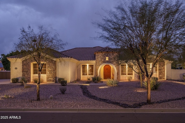 mediterranean / spanish home with stone siding, fence, a tile roof, and stucco siding