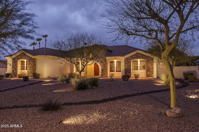 mediterranean / spanish-style house with stone siding, stucco siding, and a tiled roof