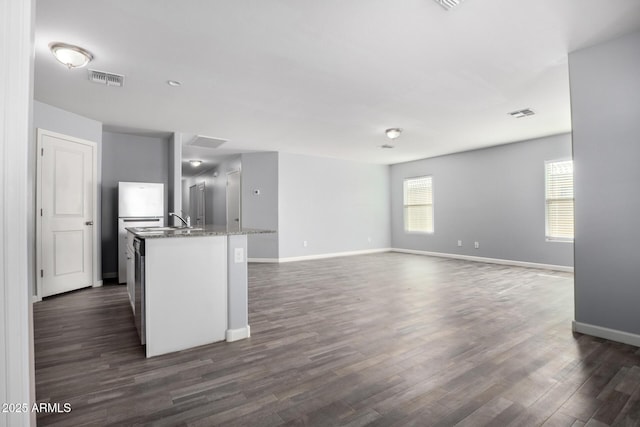 kitchen with dark wood-type flooring, white cabinetry, light stone counters, refrigerator, and an island with sink