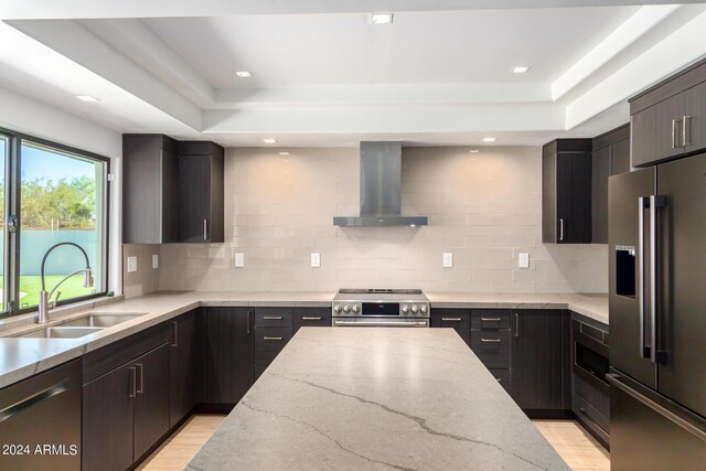 kitchen featuring high end appliances, light wood-type flooring, sink, wall chimney range hood, and decorative backsplash