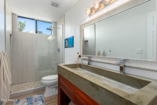 bathroom with hardwood / wood-style floors, toilet, tiled shower, and vanity