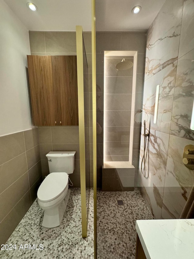 bathroom featuring tile patterned floors, toilet, a tile shower, tile walls, and vanity