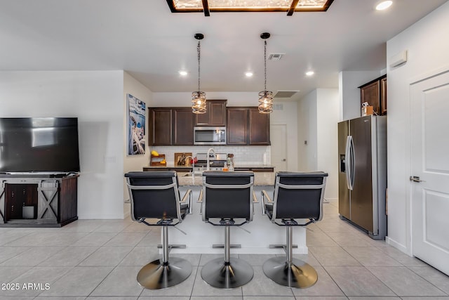 kitchen featuring a kitchen island with sink, stainless steel appliances, light stone countertops, a breakfast bar, and pendant lighting