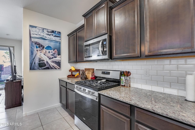 kitchen featuring light tile patterned floors, backsplash, dark brown cabinets, light stone countertops, and appliances with stainless steel finishes