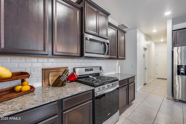 kitchen featuring light stone countertops, light tile patterned floors, decorative backsplash, appliances with stainless steel finishes, and dark brown cabinets