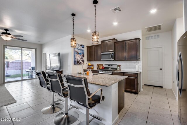 kitchen featuring stainless steel appliances, sink, light stone counters, a kitchen breakfast bar, and pendant lighting