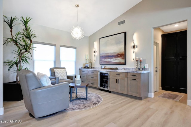 19745 N Mountain Sage Ln, Surprise, AZ 85374 - living area with beverage cooler, light wood-type flooring, high vaulted ceiling, a chandelier, and a bar
