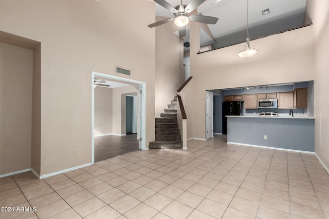 unfurnished living room featuring ceiling fan, light tile patterned floors, and a high ceiling