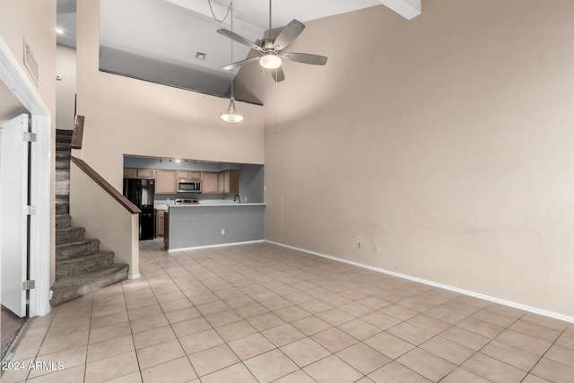 unfurnished living room with beam ceiling, ceiling fan, a towering ceiling, and light tile patterned flooring