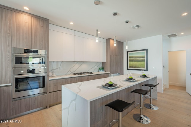 kitchen featuring stainless steel appliances, light hardwood / wood-style flooring, white cabinets, a center island, and hanging light fixtures