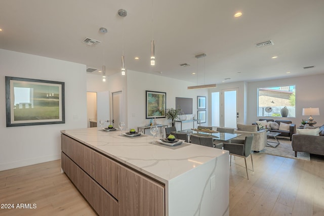 kitchen featuring light stone countertops, pendant lighting, light hardwood / wood-style flooring, and a spacious island