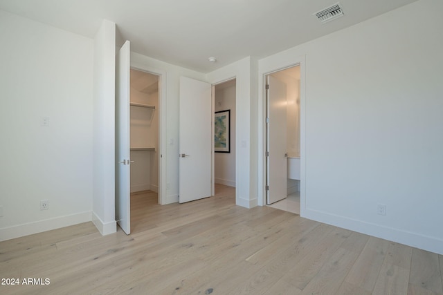 unfurnished bedroom featuring light wood-type flooring, ensuite bathroom, a spacious closet, and a closet