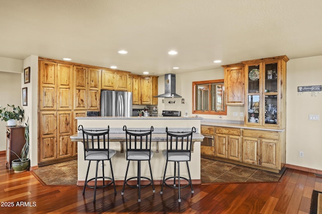 kitchen featuring dark wood-type flooring, a kitchen bar, a center island, stainless steel refrigerator, and wall chimney range hood