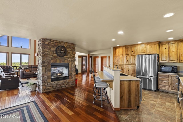 kitchen with dark hardwood / wood-style floors, a fireplace, stainless steel refrigerator, an island with sink, and a kitchen breakfast bar