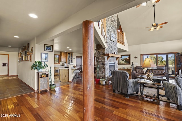 living room with a stone fireplace, dark hardwood / wood-style floors, and ceiling fan