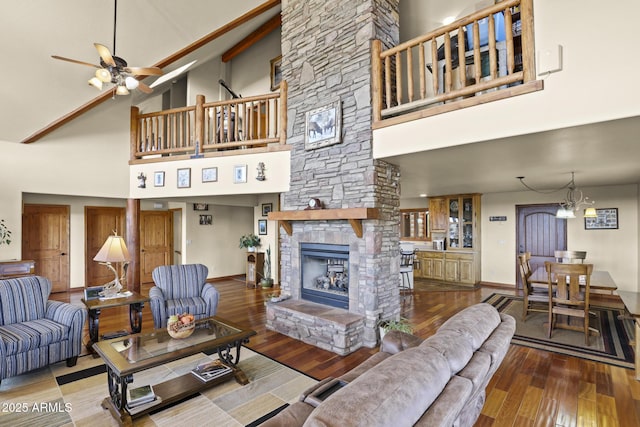 living room featuring a towering ceiling, wood-type flooring, a stone fireplace, and ceiling fan with notable chandelier