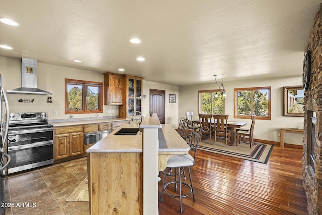 kitchen featuring a breakfast bar, decorative light fixtures, sink, double oven range, and wall chimney exhaust hood