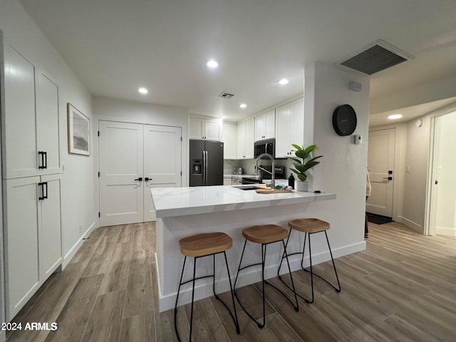 kitchen featuring sink, white cabinetry, black fridge, light hardwood / wood-style flooring, and kitchen peninsula