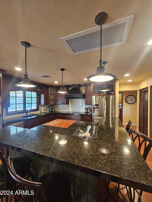 kitchen with pendant lighting, sink, a kitchen bar, stainless steel fridge with ice dispenser, and wall chimney exhaust hood