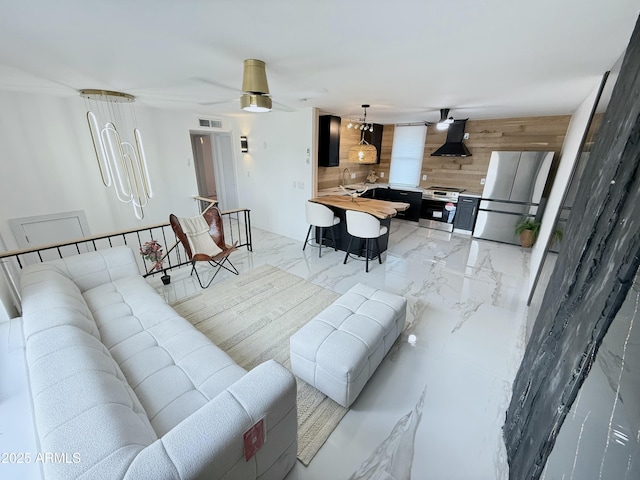 living area with a ceiling fan, wooden walls, visible vents, and marble finish floor